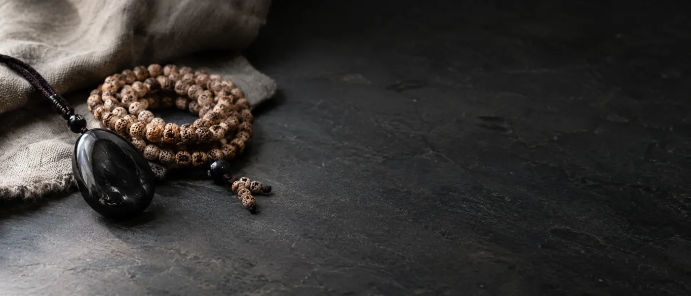 108 bodhi seed mala beads with black obsidian protection pendant on dark stone surface