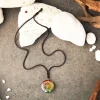 Chakra orgonite necklace laid flat on a stone surface with white pebbles, top view