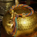 Colorful Tibetan braided bracelet coiled on a hammered brass bowl