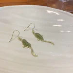 Dark green koi fish drop earrings on a plate