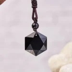 Faceted black obsidian pendant on a brown braided cord, light background