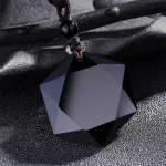 Close-up of a multi-faceted black obsidian pendant on a dark surface