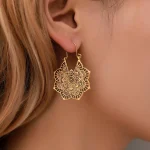 Gold lotus mandala earrings worn on an ear