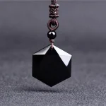 Hexagonal black obsidian pendant hanging on a dark textured background