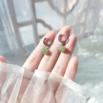 Silver huggie hoop earrings with green jade beads held in a hand