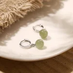 Silver huggie earrings with green jade beads on a plate