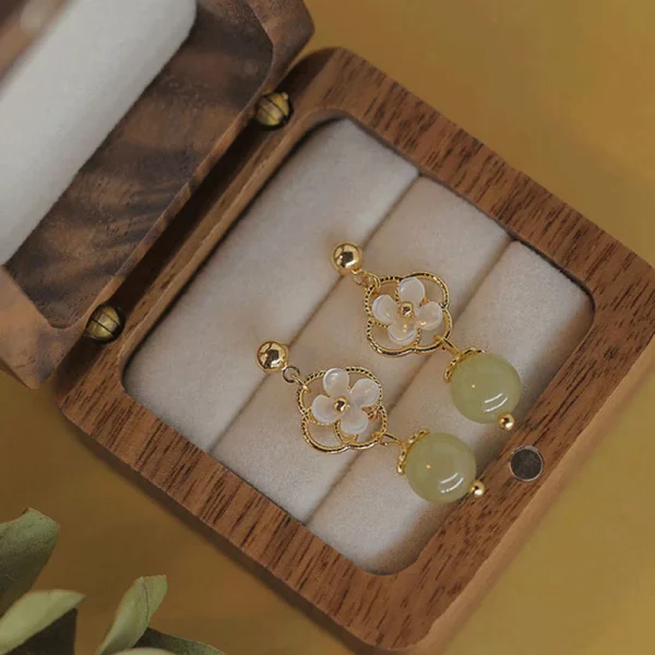 Gold drop earrings with white shell flowers and green jade beads in a wooden box