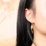 Gold koi fish jade earrings worn on an ear