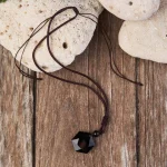 Obsidian pendant cord resting on wooden planks with smooth stones