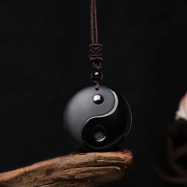 Black obsidian yin yang pendant necklace resting on a piece of wood