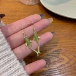 Pale green jade koi fish earrings in a hand