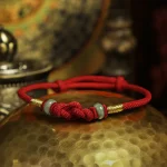Red string bracelet with jade bead resting on a hammered brass bowl