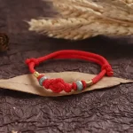Red string bracelet with jade bead resting on a dried leaf