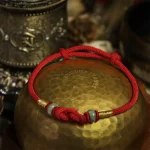 Red string bracelet with jade bead resting on a brass bowl, top view