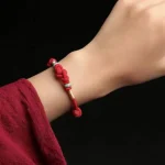 Red string bracelet with jade bead worn on a wrist with a red sleeve