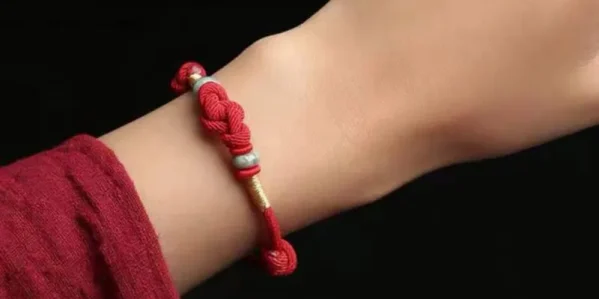 Red string bracelet with jade bead worn on a wrist with a red sleeve