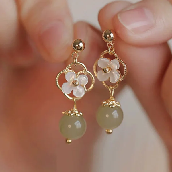 Shell flower and green jade drop earrings held in a hand