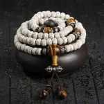 108 bodhi seed mala beads with tiger eye stones and silver accents coiled on a black stand