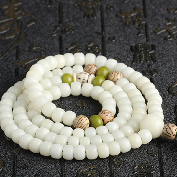 White bodhi seed mala coiled on a dark textured surface