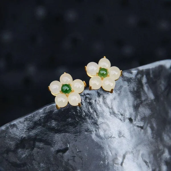 White jade flower stud earrings resting on a black stone