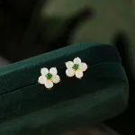 White jade flower stud earrings with green center resting on a green velvet box