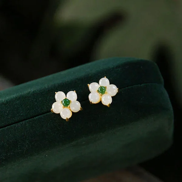 White jade flower stud earrings with green center resting on a green velvet box