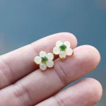 Pair of white jade flower stud earrings held between fingers