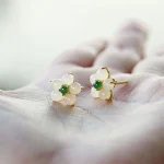 White jade flower stud earrings resting on a palm