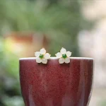 White jade flower stud earrings resting on the rim of a red cup