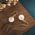White jade and gold double happiness drop earrings on wood